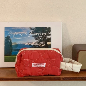Detail of red quilted cotton pouch featuring rabbit pattern stitching and woven label
