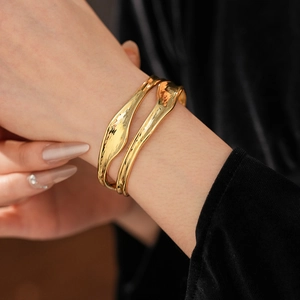Close-up of polished gold irregular layered open cuffs worn on a model's wrist