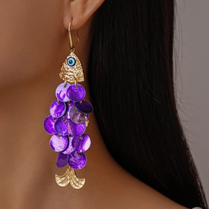 Macro detail of gold fish-shaped drop earring with purple sequins and evil eye accent