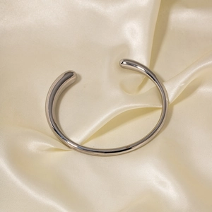 Polished silver stainless steel open bangle displayed on smooth satin fabric background