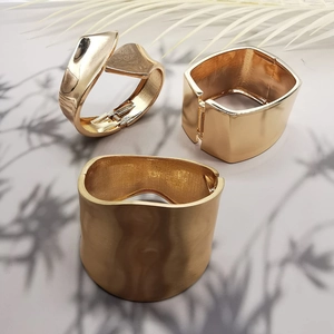 Detailed view of three gold-tone metallic bracelets with wavy and twisted geometric designs