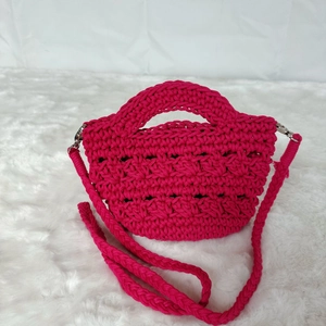 Handmade magenta crochet handbag with crossbody strap on white faux fur background