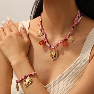 Parure de bijoux en soie rose avec pendentifs cœur et boussole dorés sur un mannequin