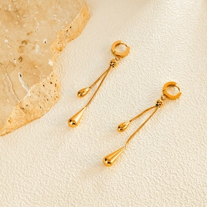 Detail of elegant gold teardrop tassel earrings on a textured minimalist background