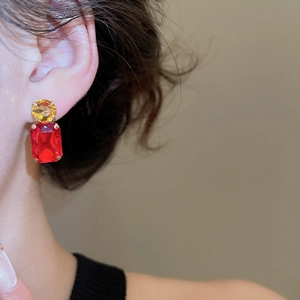 Close-up of geometric earrings with round yellow and rectangular red crystals in gold settings