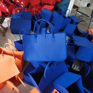 Multiple colorful felt tote bags in blue, orange and red stacked in a storage area