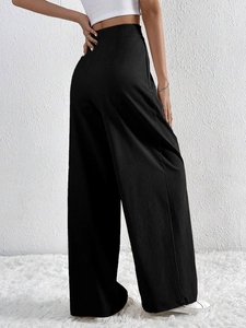 Detail of high-waist black wide-leg trousers with micro-pleated texture and drape effect
