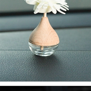 Close-up of car aromatherapy glass bottle with wooden cap and white flower diffuser
