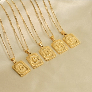 Gros plan de pendentifs rectangulaires à initiales plaqués or 18 carats avec texture soleil