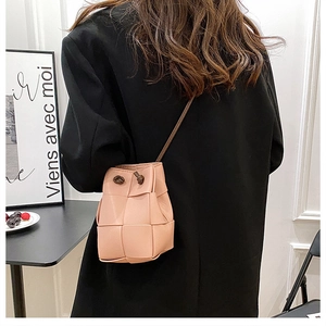 Lifestyle view of a pink hand-woven bucket bag styled with a minimalist black blazer