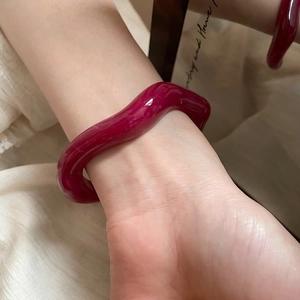 Detailed view of irregular wavy dark red resin open bangle on a woman's wrist with reflection