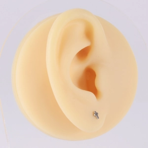 Detail shot of a small silver titanium cross stud earring on a silicone ear model