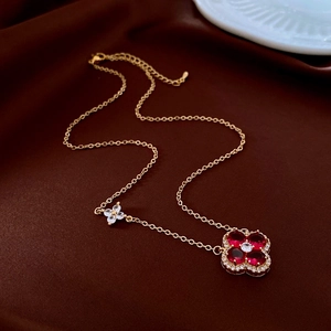 Detail of gold clover necklace with red heart-shaped stones and small crystal accents