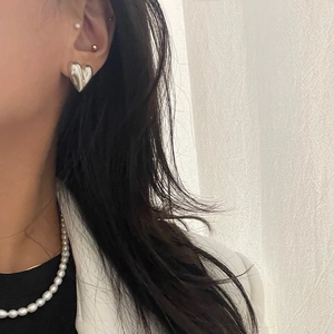 Close-up of minimalist silver heart-shaped earrings and white pearl necklace on model