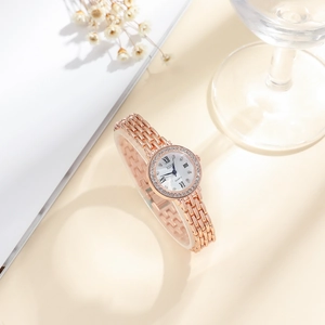 Detail of rose gold quartz watch with rhinestone bezel and Roman numerals on book