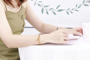 Close-up of golden stainless steel bracelet with key pendant worn by a model in lifestyle setting