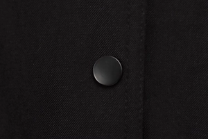 Nahaufnahme von schwarzem mattem Rundknopf und hochwertigem Twill-Stoff der Jacke