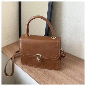 Detail of brown PU leather handbag with golden metal lock and stitching on wooden shelf