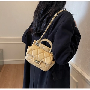 Detail of beige quilted crossbody bag featuring gold hardware lock and leather chain strap