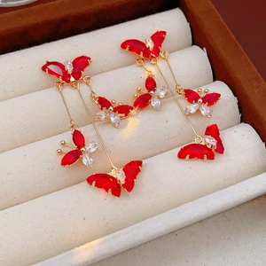 Detail shot of golden butterfly tassel earrings with red zircons in a jewelry box