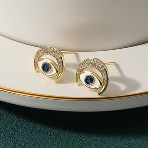 Elegant gold evil eye stud earrings with blue gemstone and diamonds on a white plate