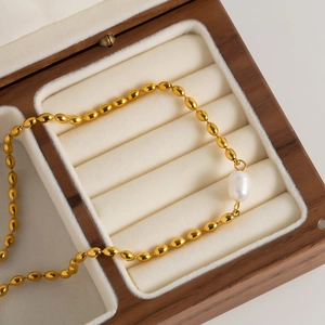 Detailed view of a gold oval bead chain with a baroque pearl pendant in a wooden box