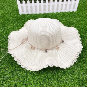 Détail du bord ondulé du chapeau de paille avec perles grises et pendentifs en coquillages