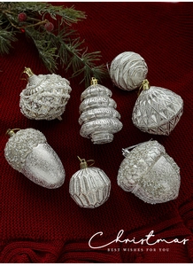 Dettaglio di ornamenti natalizi in argento con glitter e perle su maglia rossa