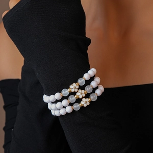 Detail of three-piece beaded bracelet set with white enamel flowers on a model's wrist