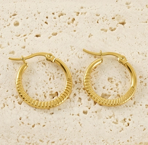 Close-up of 18K gold plated titanium hoop earrings with radial grooved texture on travertine