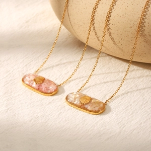 Detailed macro view of oval gold shell pendants with pink resin inlay on soft fabric