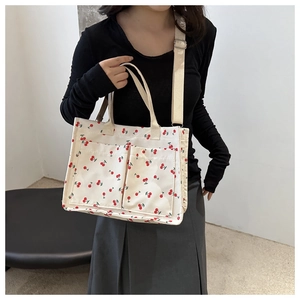Close-up of a cream canvas tote bag featuring red cherry prints and two front pockets