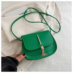 Detail of green leather saddle bag with gold trim and tassel on a beige blazer