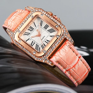 Close-up of square rose gold watch with rhinestone bezel and orange leather strap