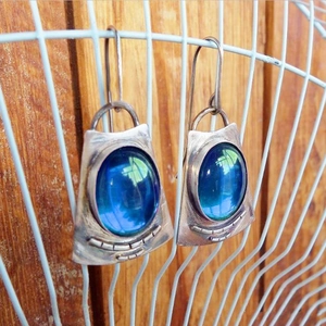 Vintage silver oval moonstone drop earrings with blue-green stones on a dark wood background