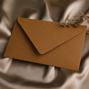Detailed texture of brown linen envelope on champagne silk with dried floral decor