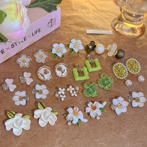 Collection of pearl stud earrings with floral and clover designs on a lifestyle background