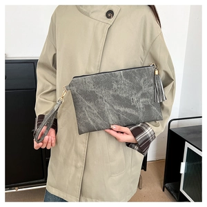 Grey marble texture clutch bag with tassel detail held by model in a trench coat