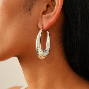 Close-up of a silver-toned ribbed oval earring featuring textured croissant style details