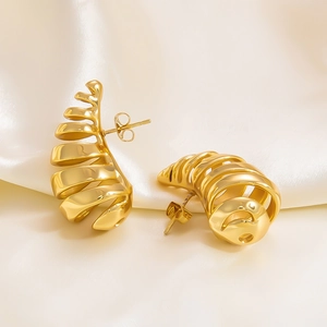 Macro shot of gold hollow spiral stud earrings on white silk fabric background
