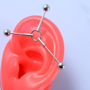 Close-up of a silver industrial barbell with triple bar design on a pink ear model