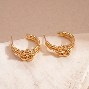 Détail de boucles d'oreilles dorées en forme de nœud en C sur une pierre texturée