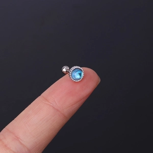 Macro view of a 20G stainless steel moonstone stud earring shown on a fingertip