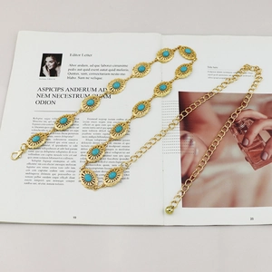 Elegant gold metal waist chain with sunburst motifs and turquoise stones on a magazine