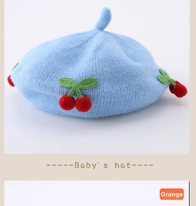Detail of light blue baby knitted beret with red cherry decor and small top tail