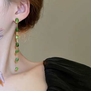 Detail of long emerald green tassel earrings with gold chain on model showing elegant drape