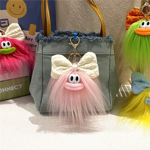 Dettaglio portachiavi mostro di peluche con fiocco su borsa in denim con colori vivaci