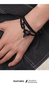 Detail of a black woven rope bracelet with a matte black whale tail metal clasp