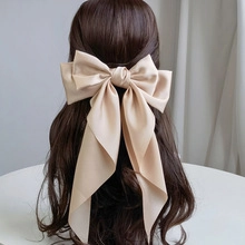 Detail of a large champagne satin bow hairclip with long ribbons on wavy brown hair