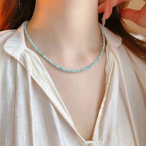 Close-up of a delicate gold plated necklace with light blue faceted beads on a model